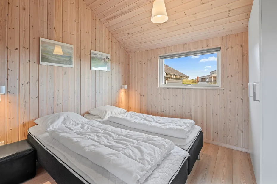 Un dormitorio revestido de madera con camas bajo una ventana.