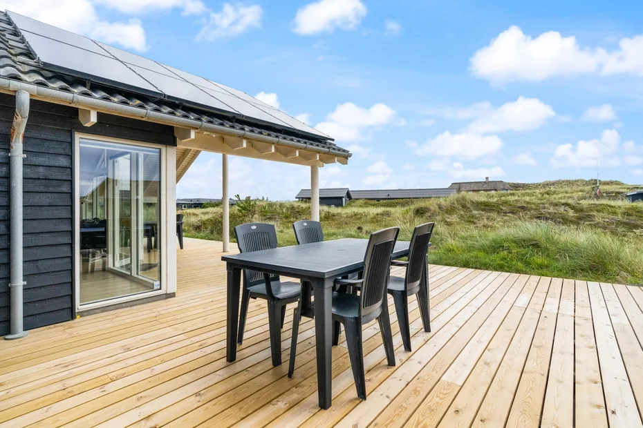 Una terraza de madera junto a una casa tiene una mesa de comedor y sillas.