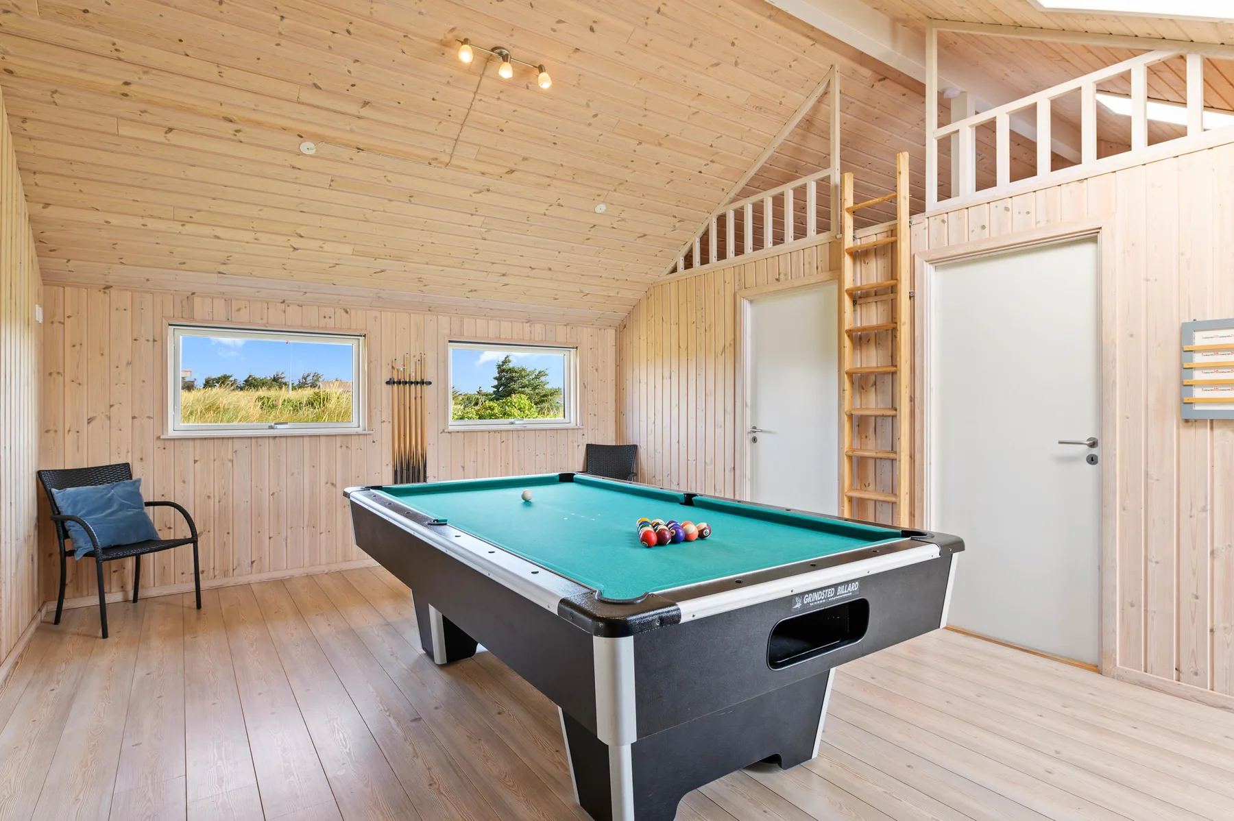 Sala de juegos con una mesa de billar y una silla junto a las ventanas.
