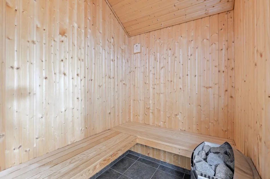 Una sauna revestida de madera con bancos en L y una estufa de piedras.
