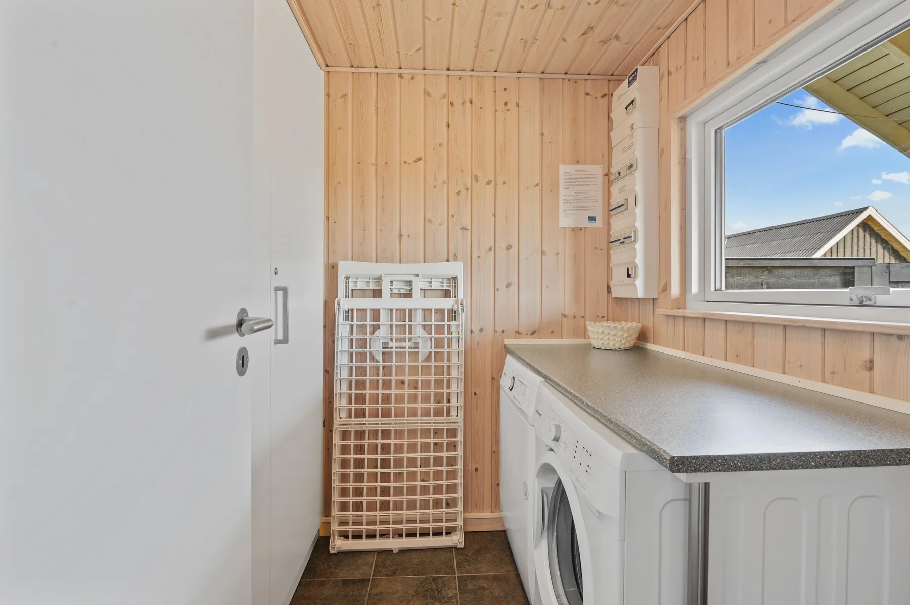 Lavadero con una lavadora, un cesto para ropa y una ventana.