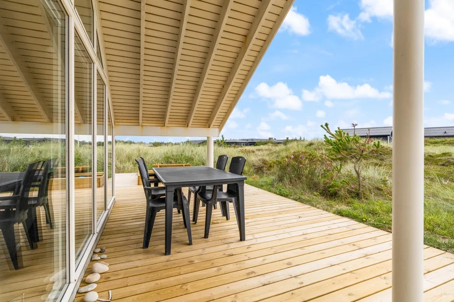 Una terraza de madera cubierta con una mesa de comedor exterior da a dunas cubiertas de hierba.