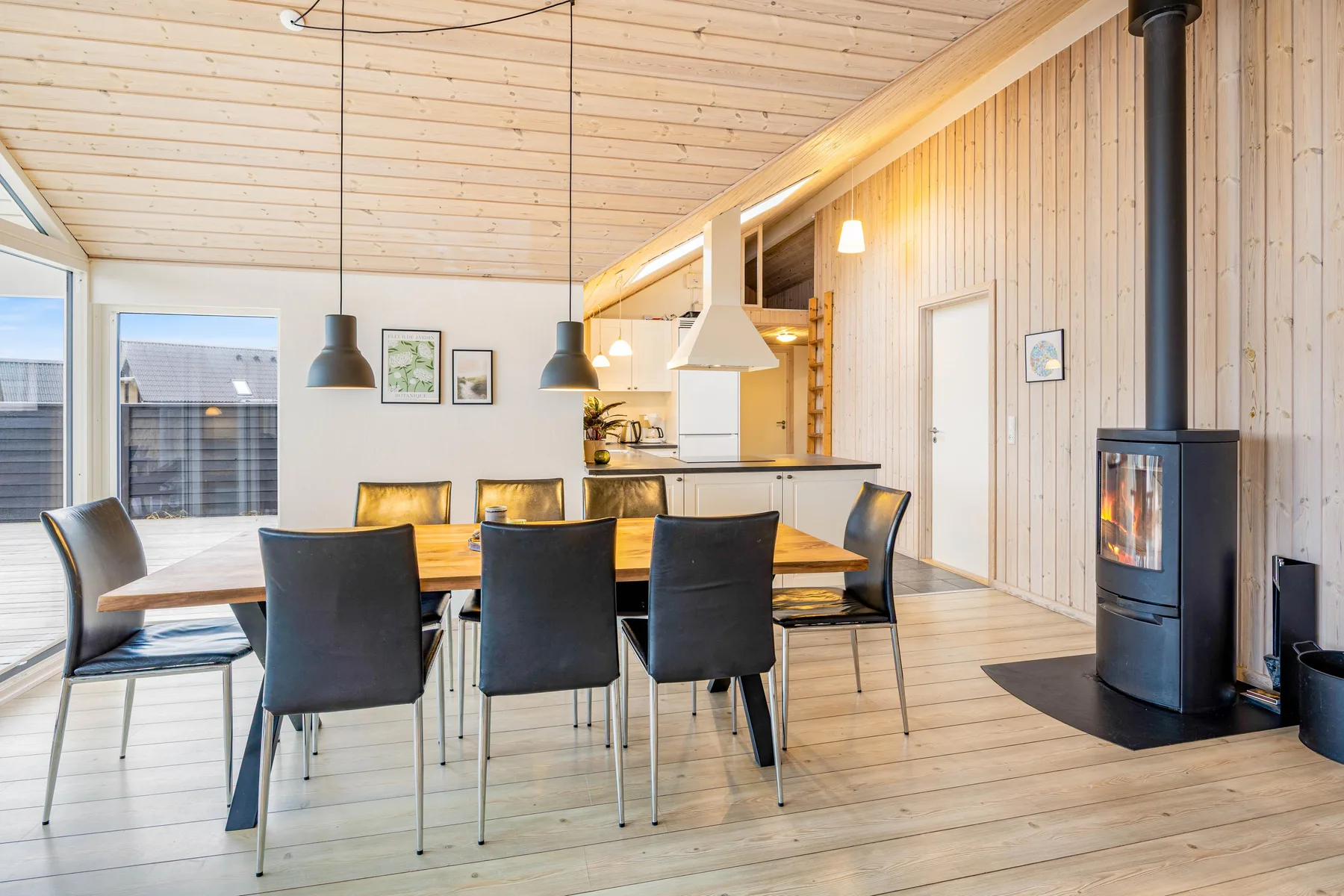 Comedor con una mesa de madera, asientos oscuros y una estufa negra.