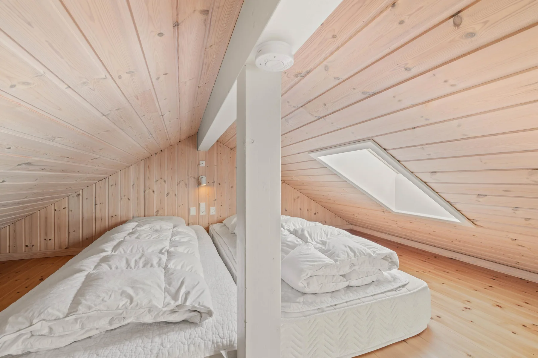 Zona para dormir con camas bajo un techo inclinado de madera.