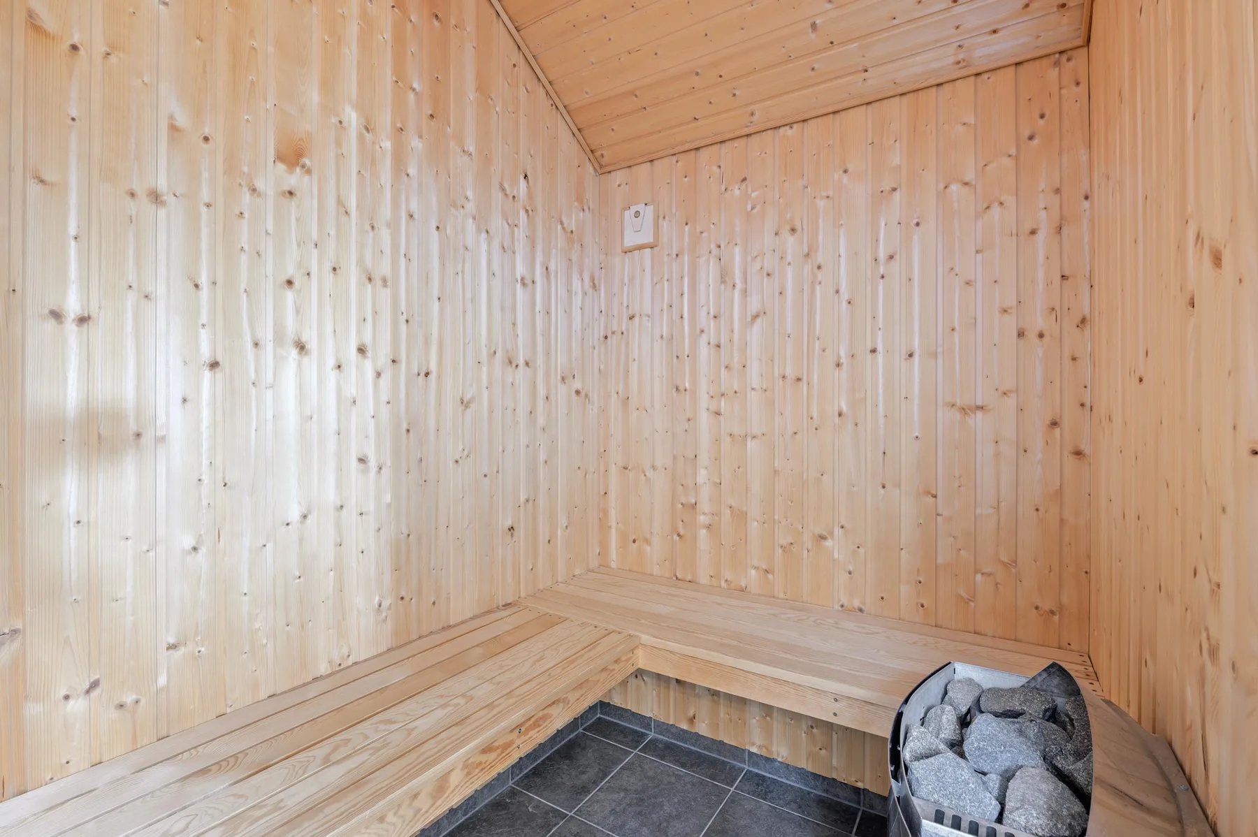 Una sauna revestida de madera con bancos y un calentador de piedras.