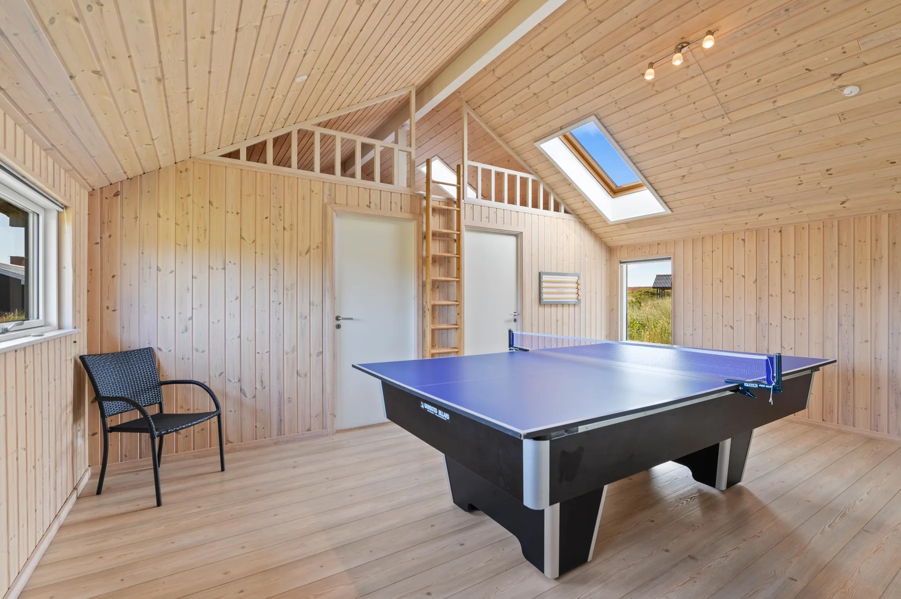 Una luminosa sala de juegos con una mesa de ping-pong azul y una silla.