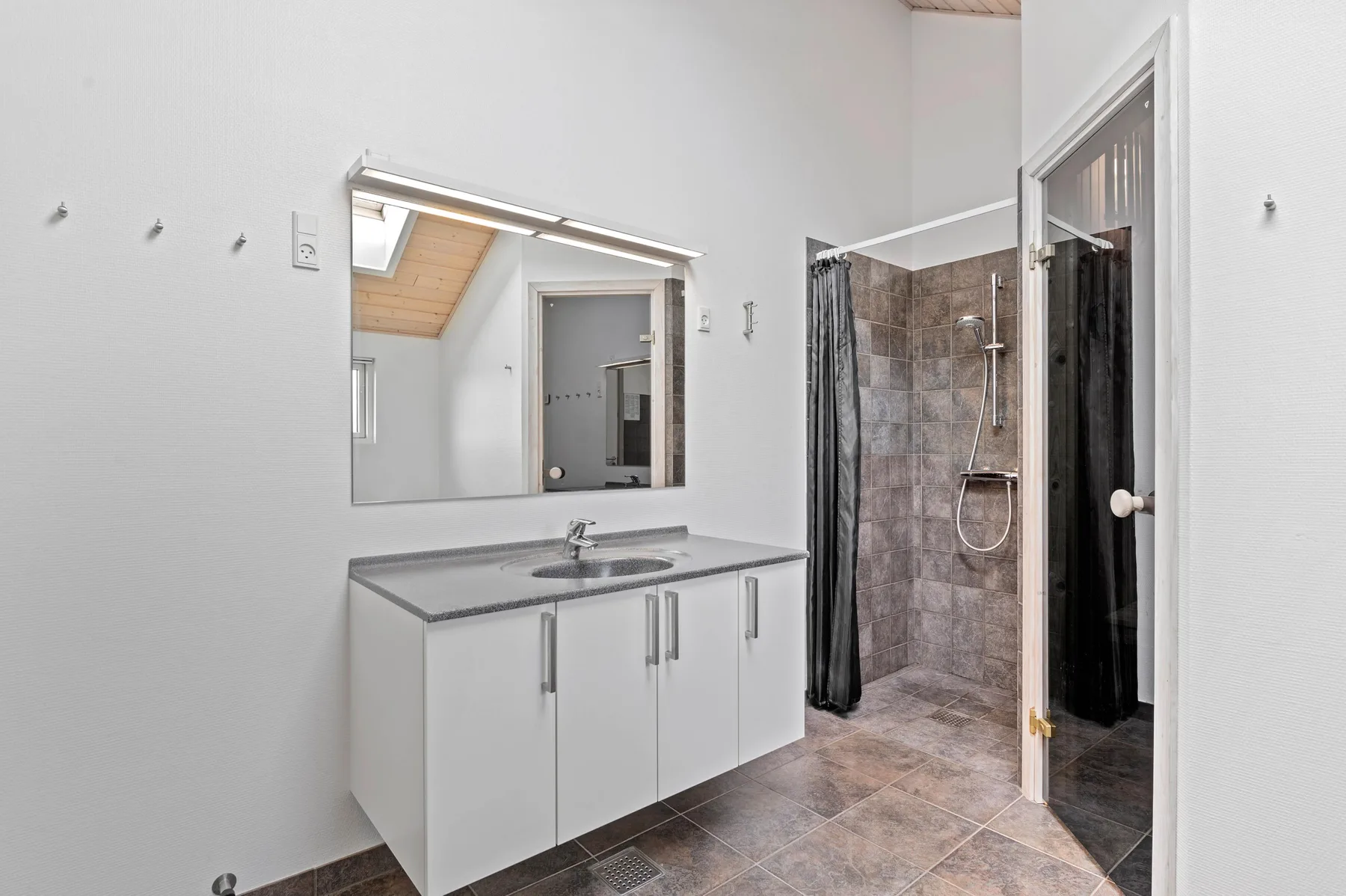 Un baño con lavabo, espejo grande y ducha con azulejos.