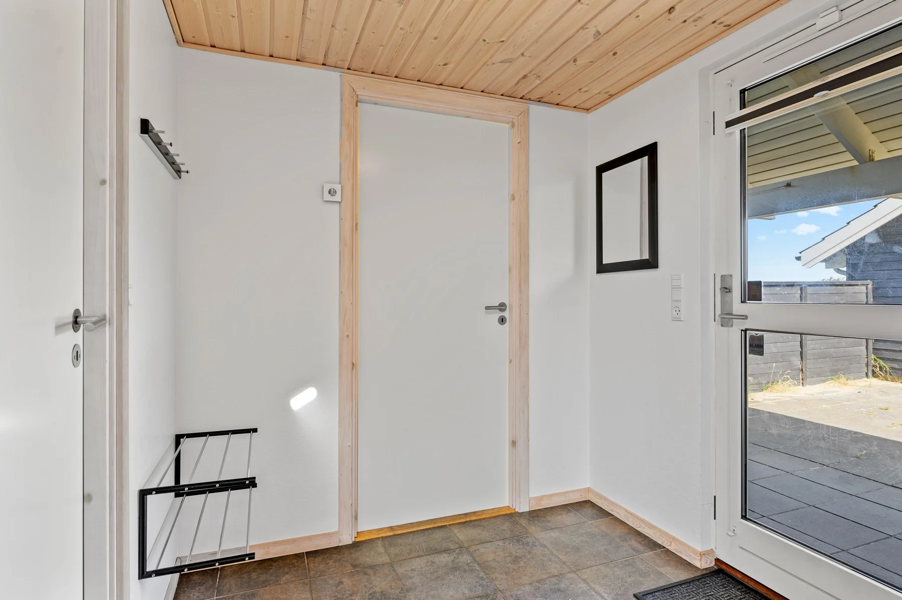 Un recibidor luminoso con una puerta blanca y ventanas que dan a una terraza.