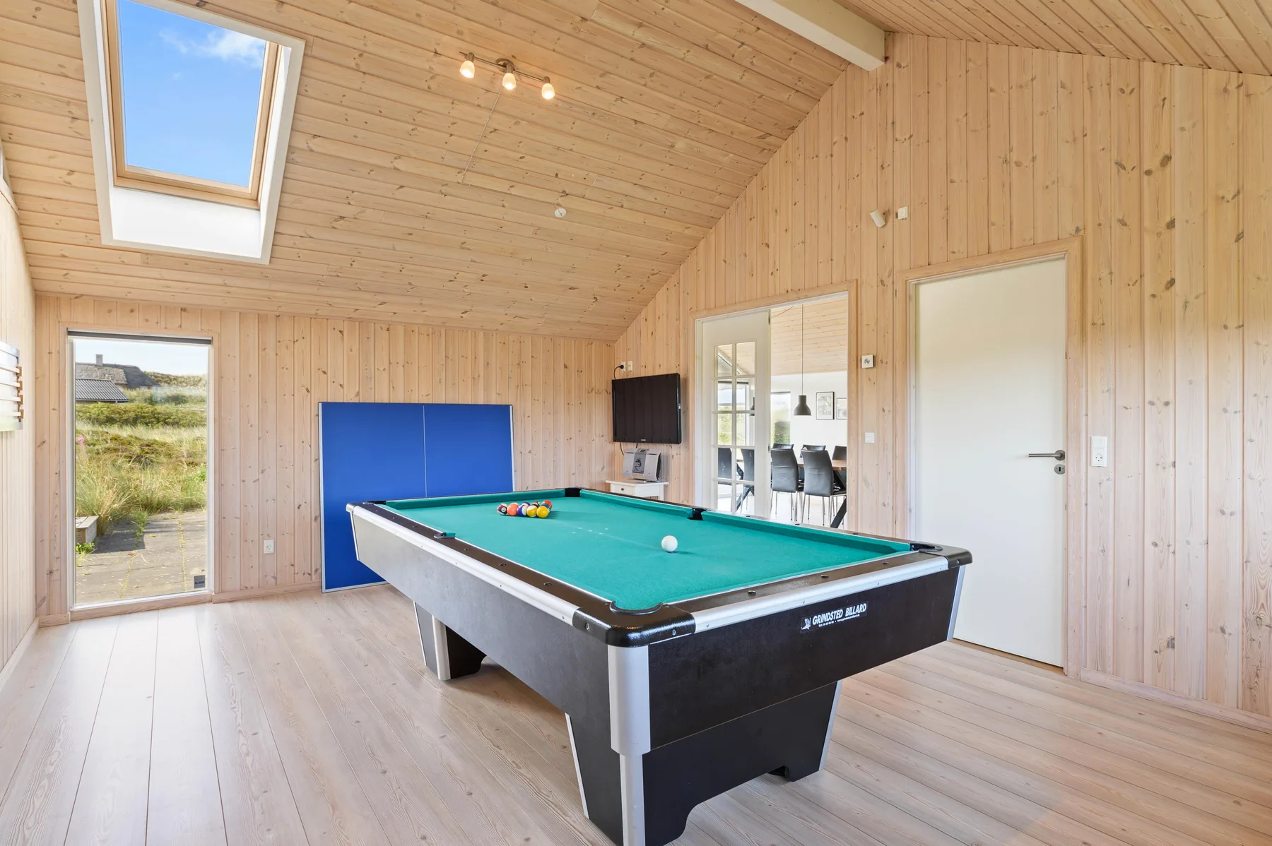 Una luminosa sala de juegos revestida de madera con una mesa de billar bajo una claraboya.