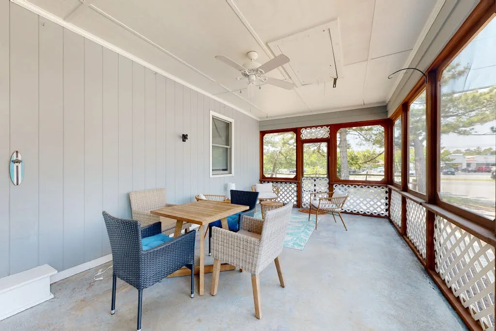 A bright enclosed porch with a dining table and wicker seating.
