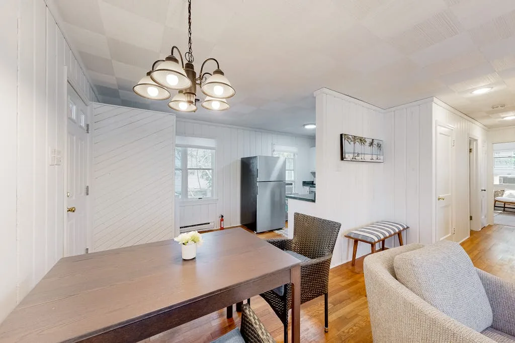 A bright dining area opens onto a kitchen, with a wooden table and chairs.