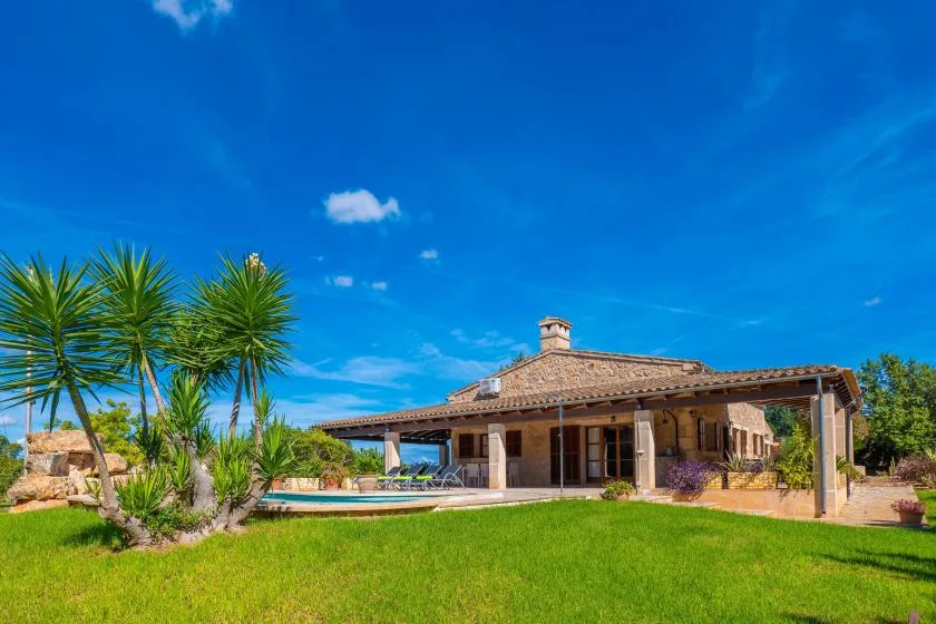 Una casa de una planta con techo de tejas está junto a una piscina y un césped.