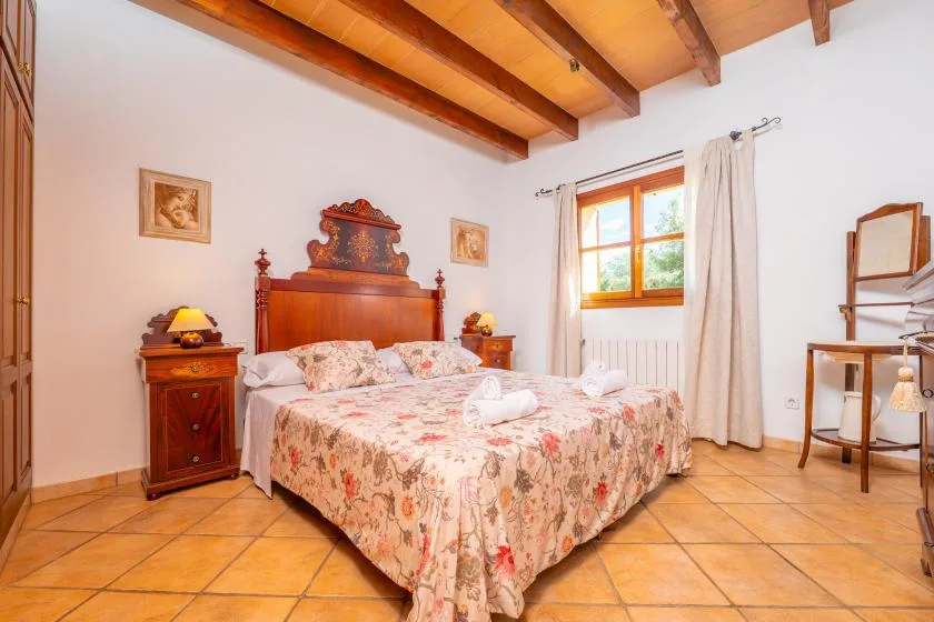 Un dormitorio con cama de madera, ropa de cama estampada y vigas expuestas en el techo.