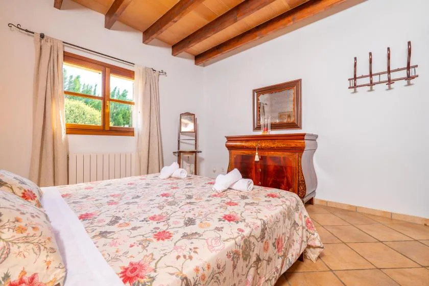 Un dormitorio con una colcha floral, una chimenea de madera y vigas vistas en el techo.