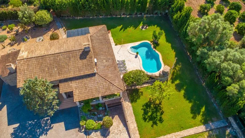 Vista aérea de una casa con tejado de tejas, césped verde y piscina.