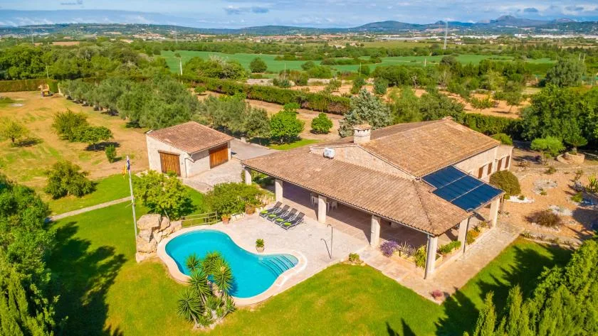 Una casa de campo con techo de tejas está junto a una piscina y un césped verde.