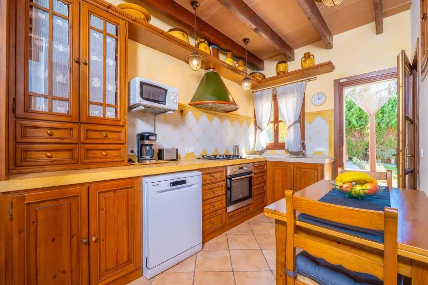 Una cocina de tonos cálidos con armarios de madera, una mesa y vistas al jardín.