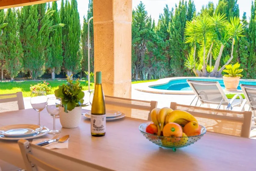 Una mesa de comedor en el patio con fruta da a una piscina y un jardín.