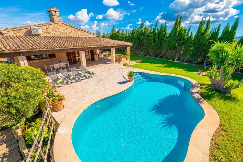 Una piscina junto a una casa con techo de tejas y asientos en el patio.