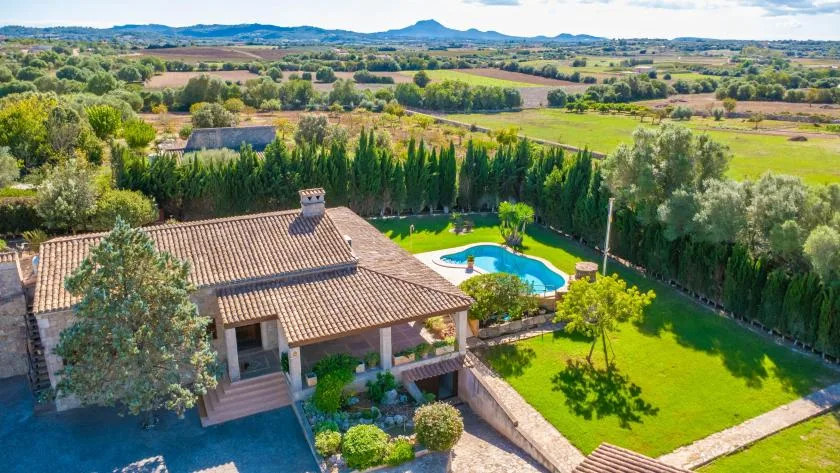 Una casa y una piscina están junto a un césped verde, con campo abierto al fondo.