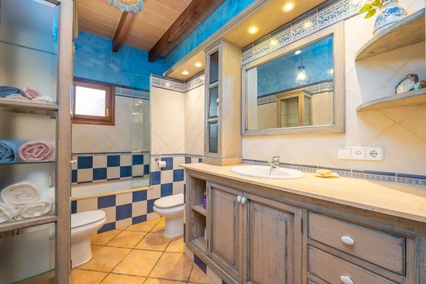 Un baño con azulejos, un tocador largo, un espejo y un lavabo blanco.