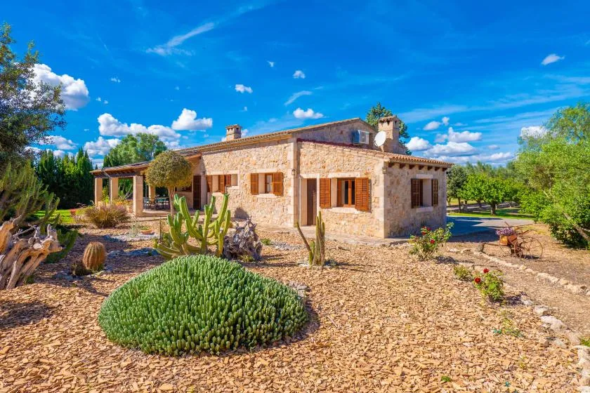 Una casa de piedra se alza en un jardín paisajístico bajo un cielo azul despejado.
