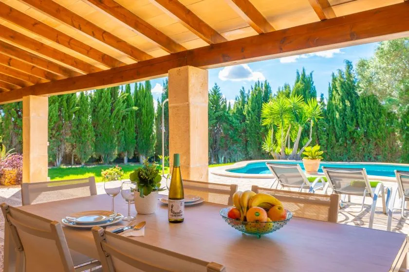 Una zona de comedor al aire libre cubierta da a una piscina y un jardín verde.