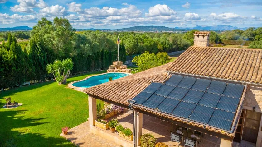 Una casa con tejado de tejas y paneles solares da a un césped verde y una piscina.
