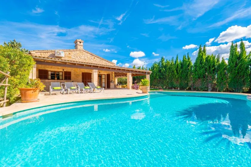 Una piscina al aire libre junto a una casa baja con patio cubierto.