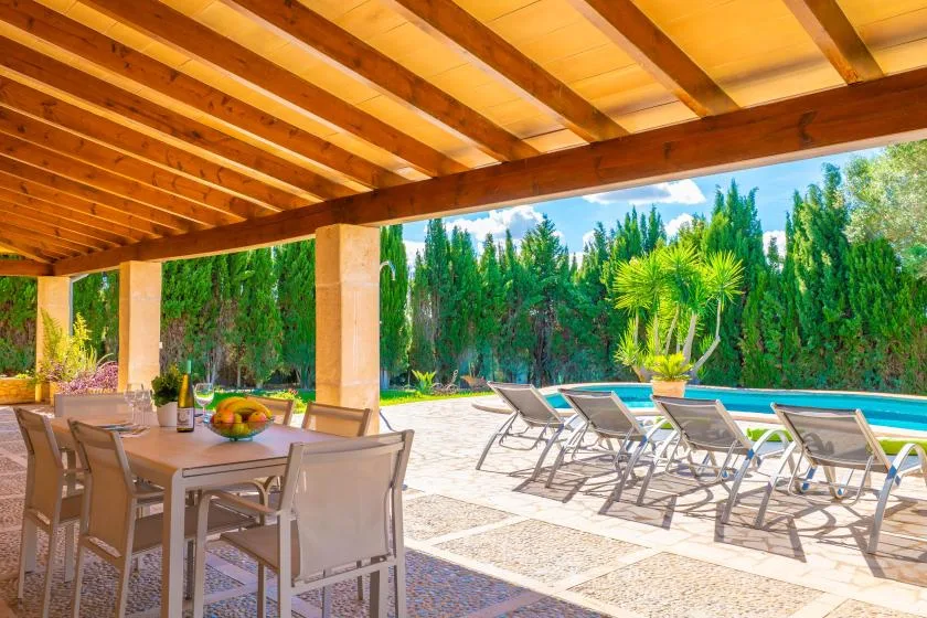 Un comedor exterior cubierto da a un patio soleado con asientos junto a la piscina.