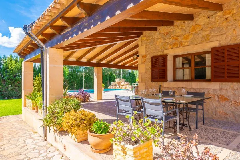 Una zona cubierta para comer al aire libre, con mesa y sillas junto a un muro de piedra.