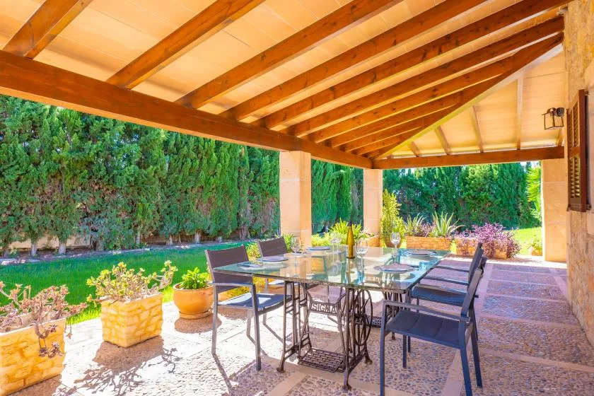 Comedor exterior cubierto con una mesa de vidrio y un jardín al fondo.
