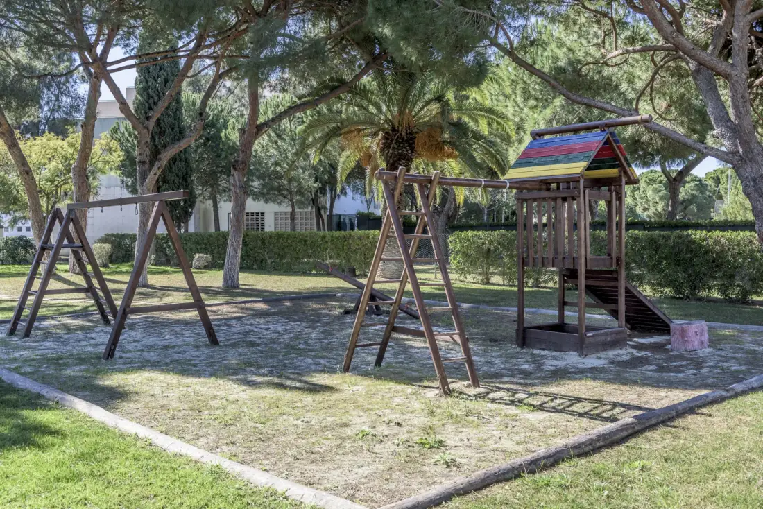 Una zona de juegos al aire libre con columpios y una pequeña estructura bajo los árboles.