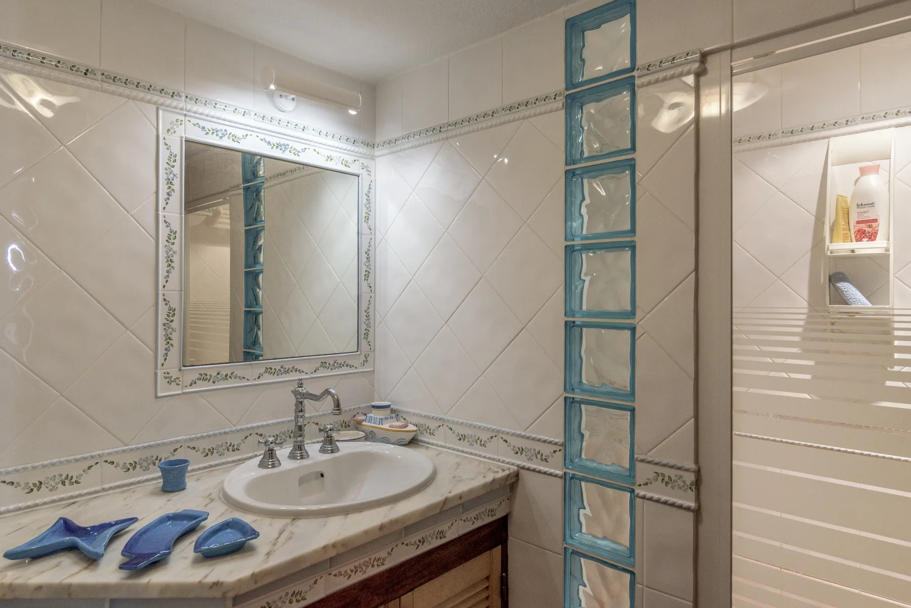 Un baño alicatado con lavabo, espejo y mampara de ducha.