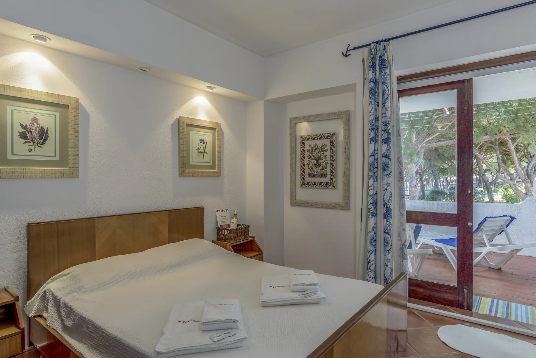 Un dormitorio con una cama doble, cuadros enmarcados y puertas de cristal que dan a un patio.