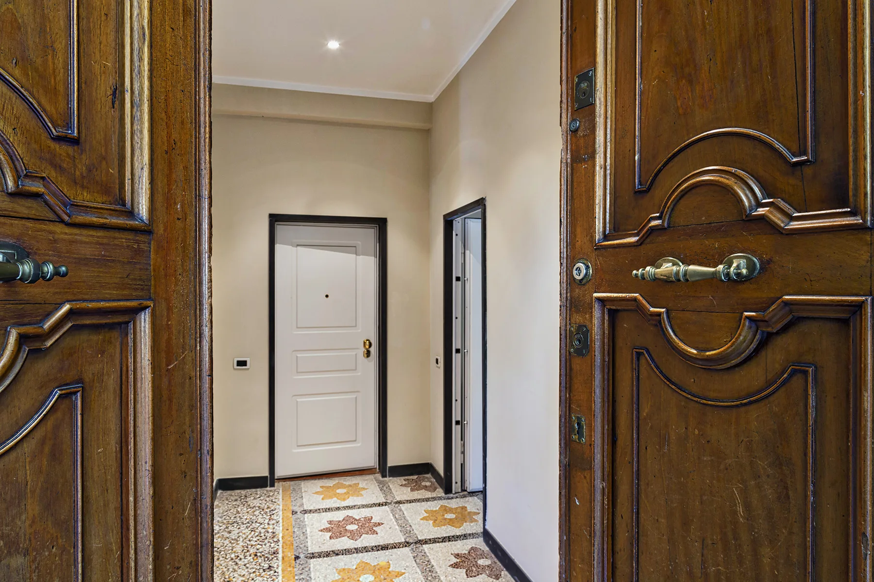 Un recibidor interior con una puerta blanca y suelo de baldosas estampadas.