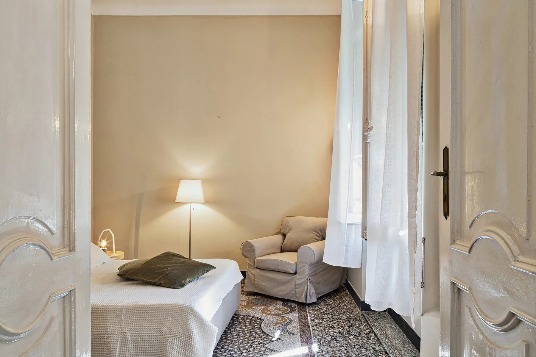 Un dormitorio con una cama, un sillón y una lámpara de noche encendida.