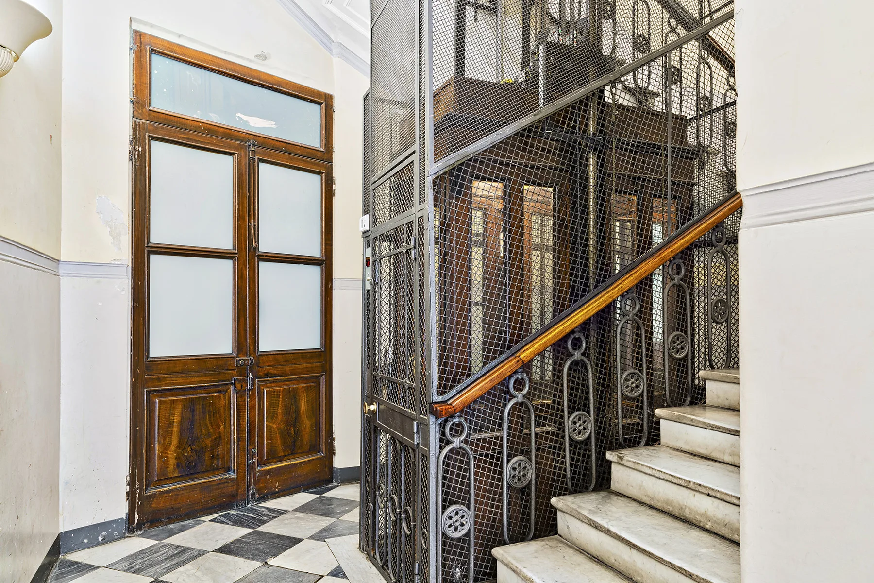 Una escalera interior con barandilla metálica junto a una puerta doble de madera.