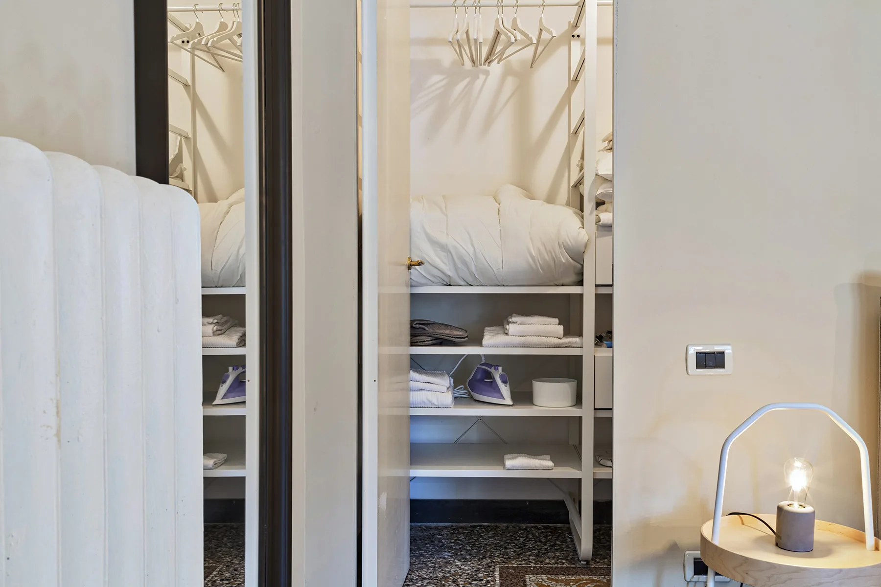 Un armario de dormitorio tiene estantes abiertos, espacio para colgar y ropa de cama doblada.