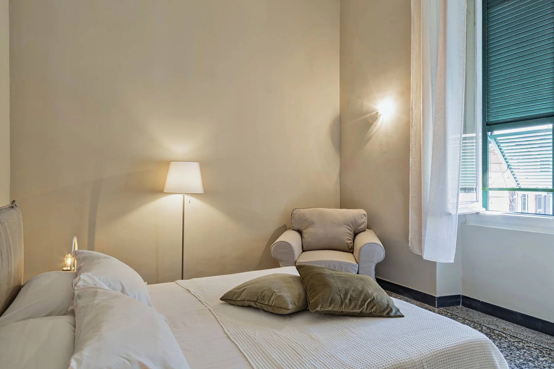 Un dormitorio con una cama, una lámpara de pie y una ventana con cortinas.