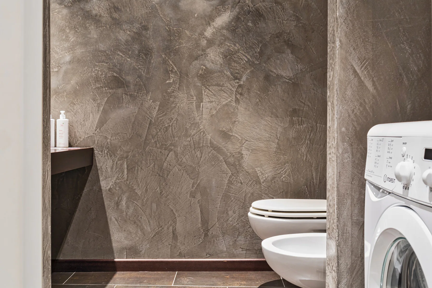 Un baño con inodoro, lavabo y lavadora junto a paredes texturizadas.