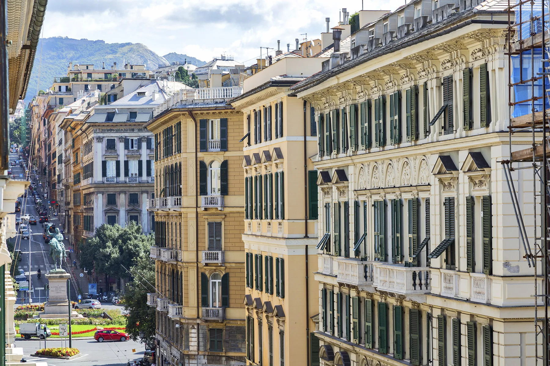 Una calle urbana flanqueada por edificios ornamentados de varios pisos, con colinas a lo lejos.