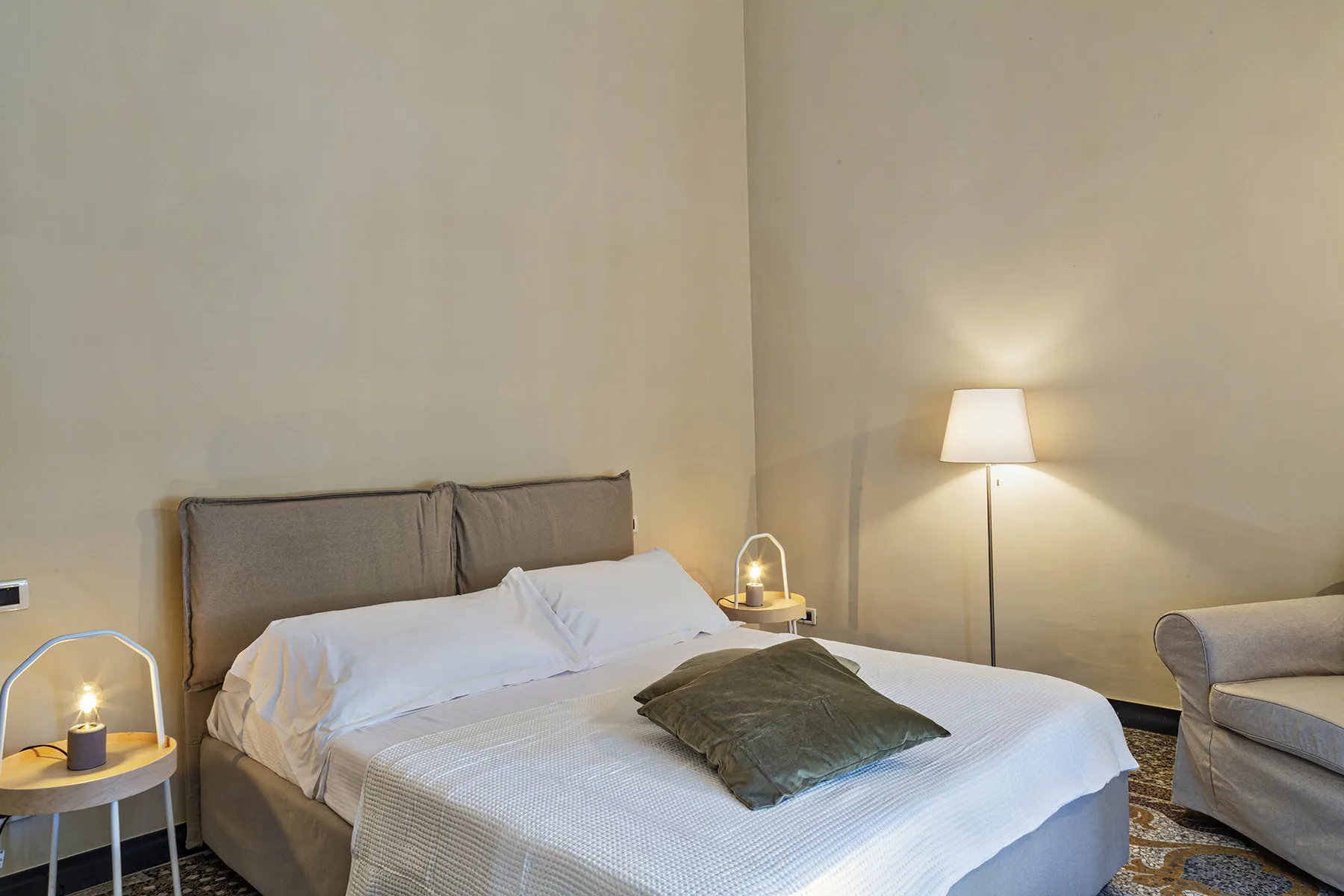 Un dormitorio con una cama, ropa de cama blanca y una lámpara de pie al lado.