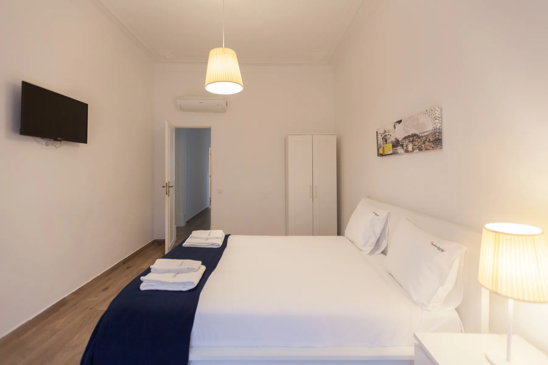 A bedroom with a large bed, white bedding, and a wall-mounted television.