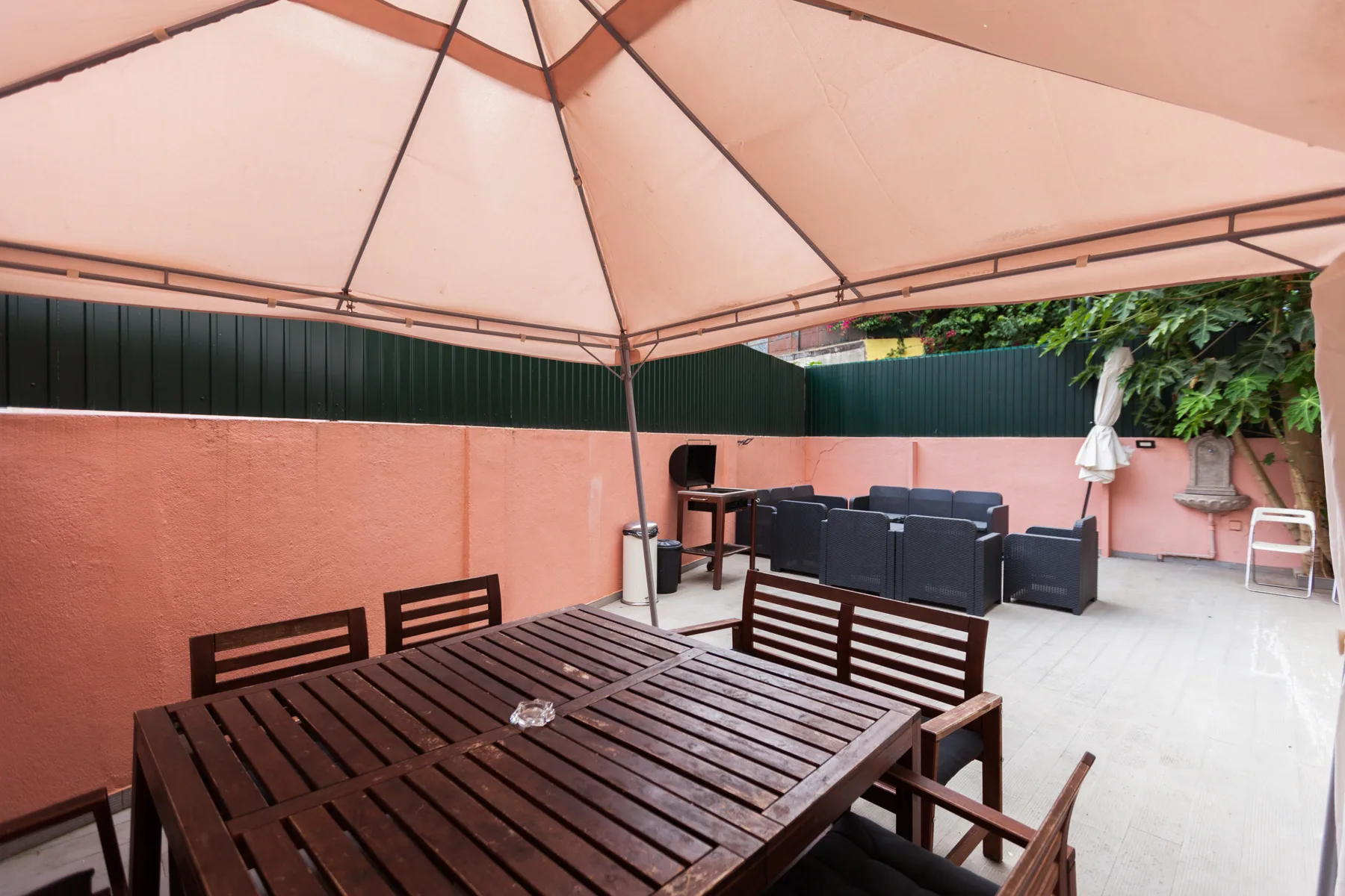 An outdoor patio has a large canopy, wooden seating, and dark lounge furniture.