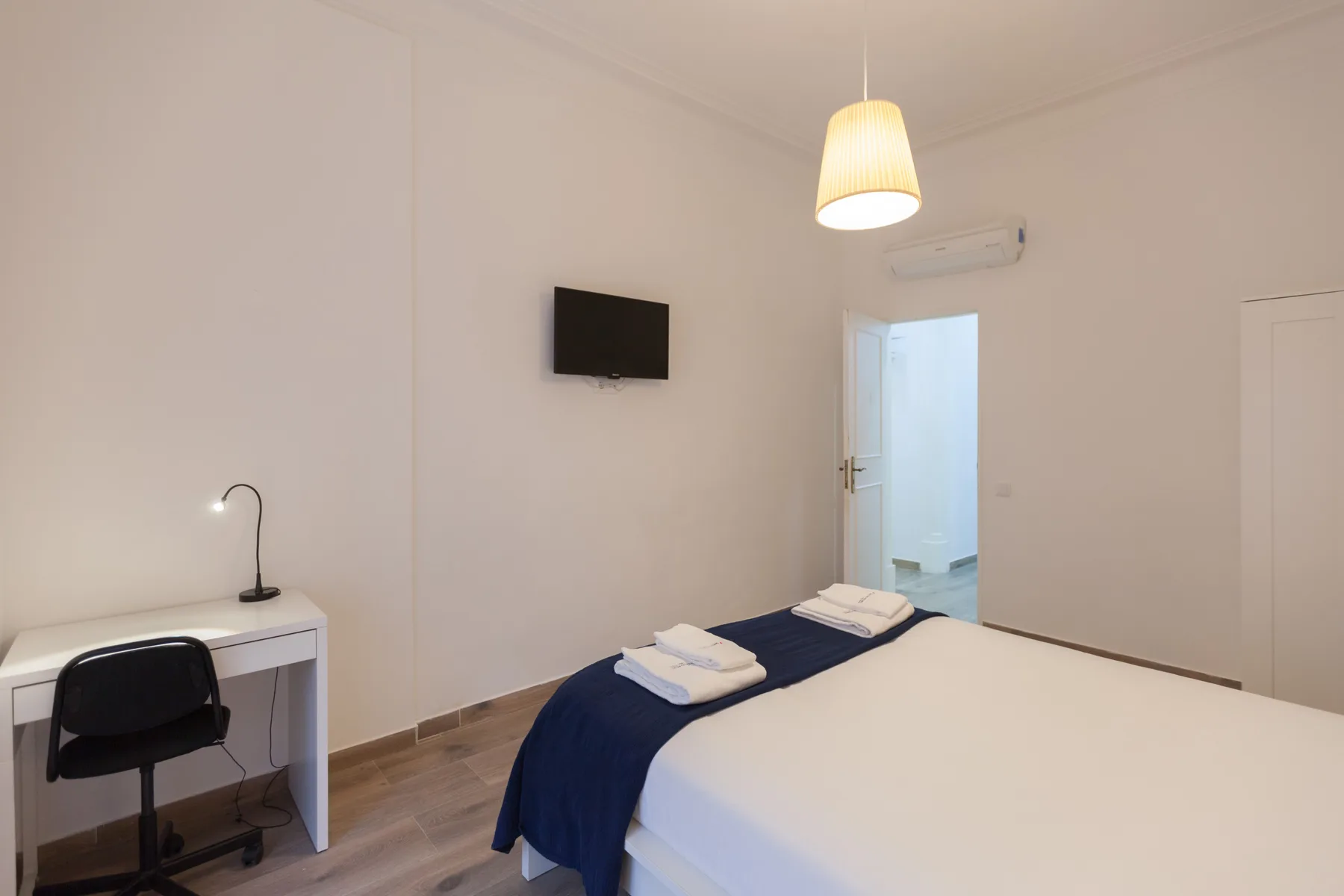 A bedroom with a bed, desk, and wall-mounted television.