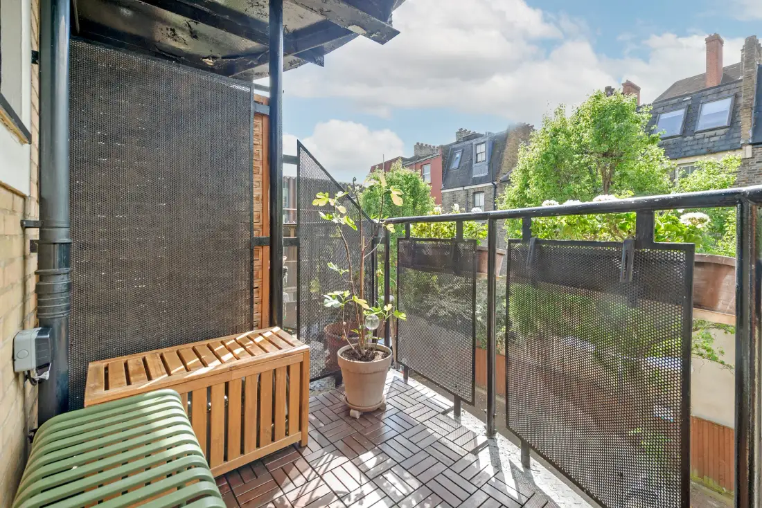 A small balcony with a wooden bench, potted plant, and mesh railing.