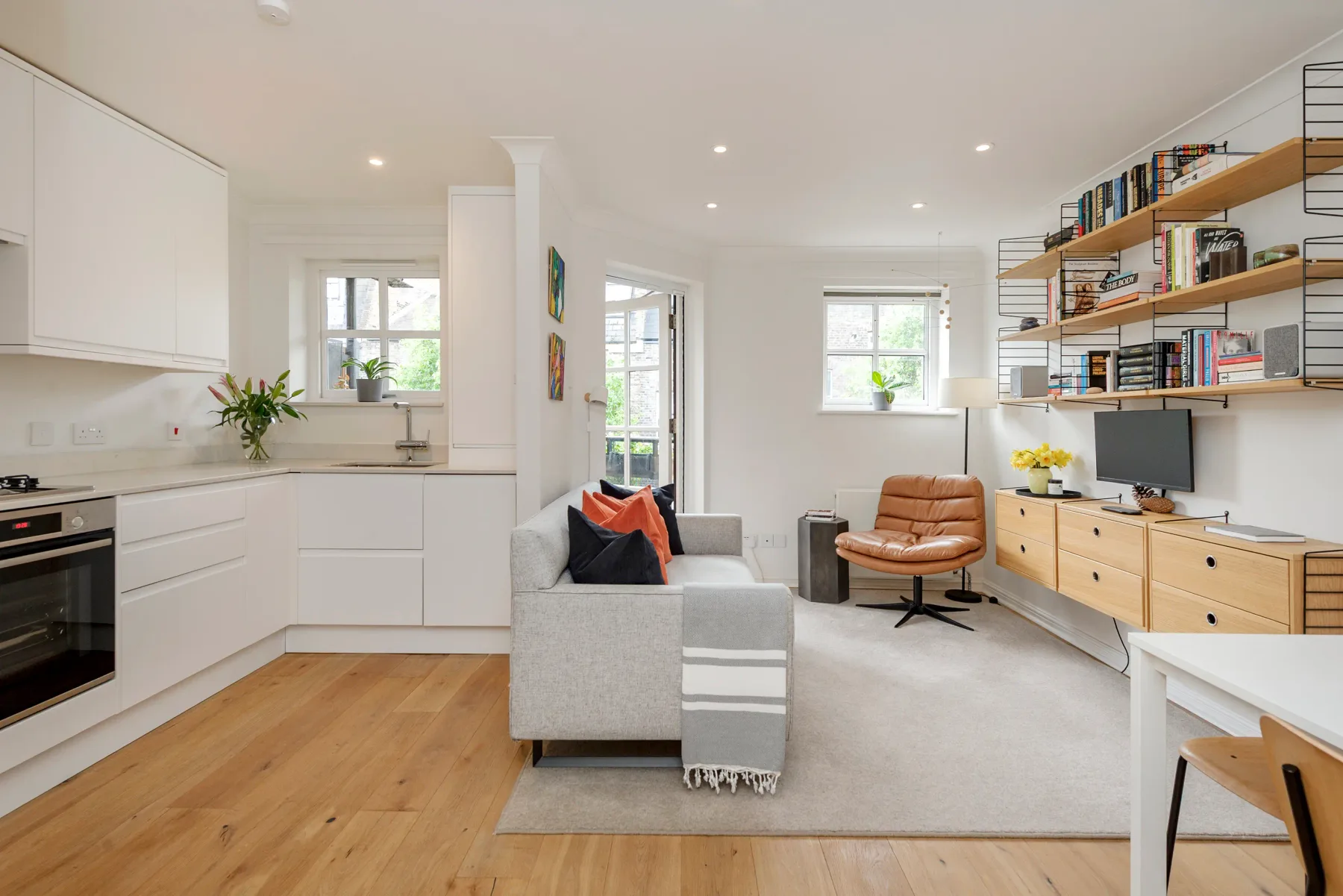 Bright open-plan living room with a kitchen, seating, and bookshelves.