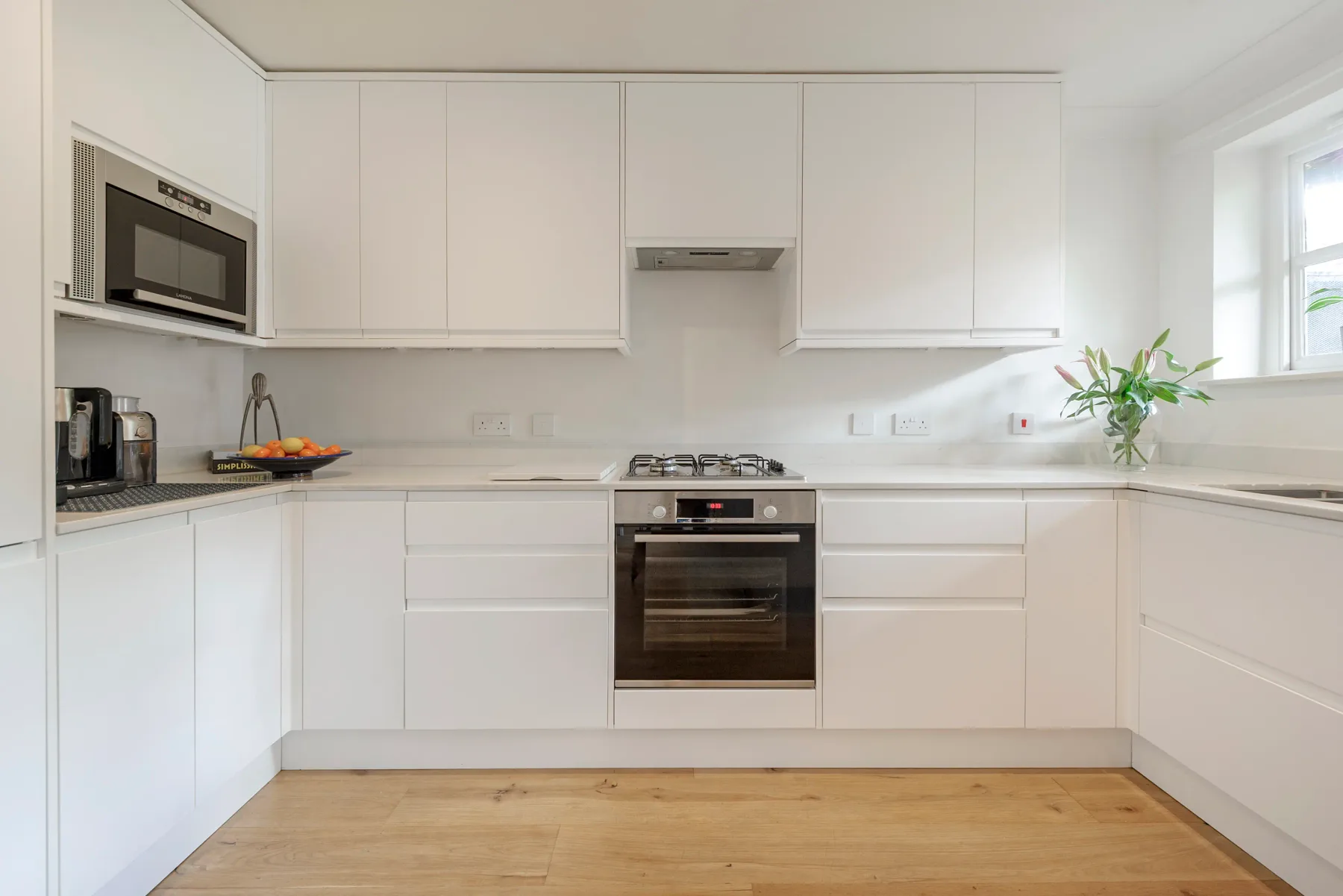 A bright white kitchen with built-in appliances and light wood flooring.