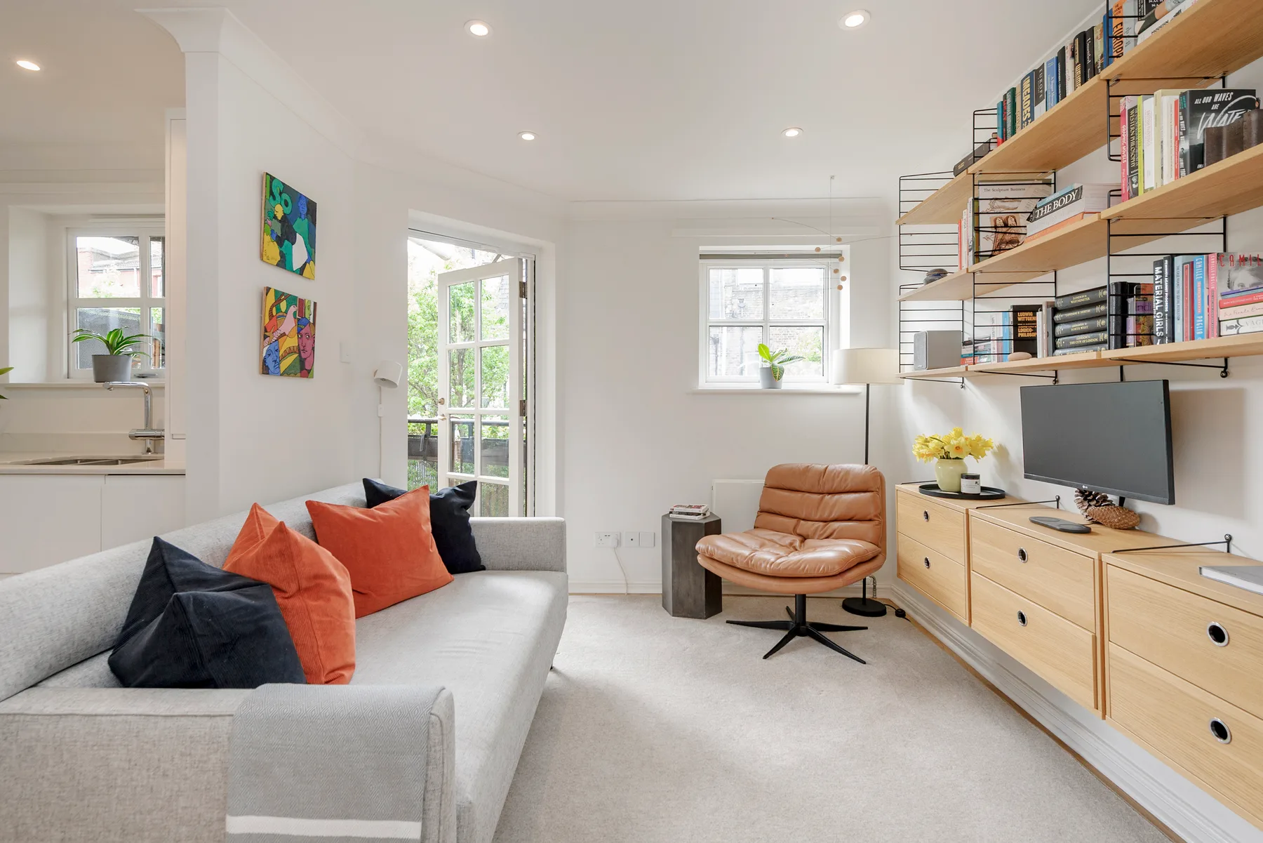 A bright living room with a sofa, lounge chair, and wall of bookshelves.